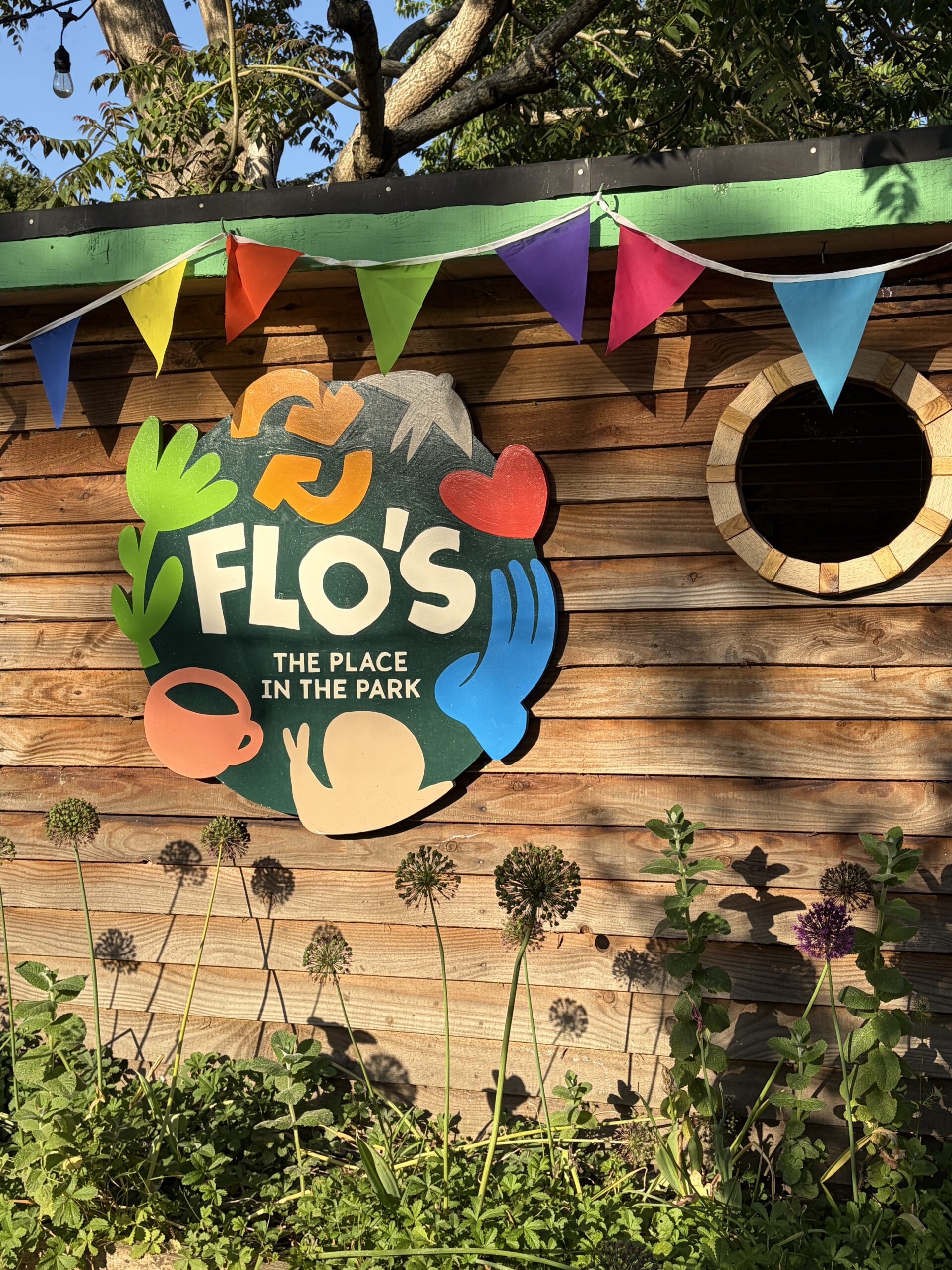 Flo's Hatch outdoor café kiosk at Flo's Place in the Park, Florence Park, with bunting, garden planting and a lunch table in the foreground.